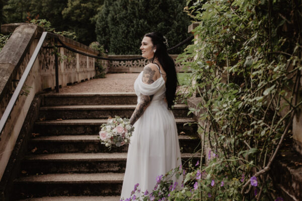 Braut steht mit Blumen auf einer Treppe im Schlosspark Altenstein