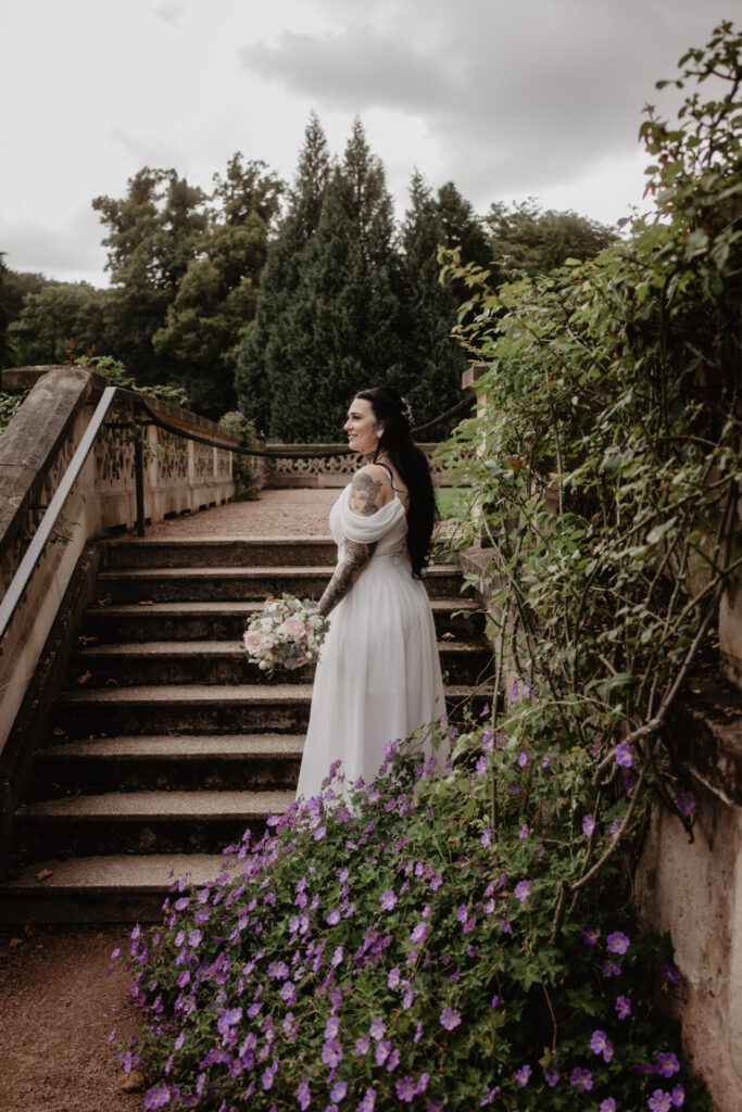 Braut steht mit Blumen auf einer Treppe im Schlosspark Altenstein