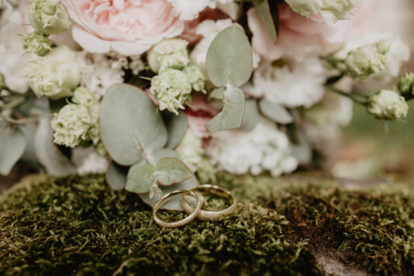 Eheringe im Moos vor einem Brautstrauß mit rosa Blumen