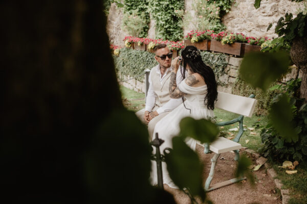 Brautpaar sitzt auf einer Bank im Schlosspark Altenstein zwischen Blumen